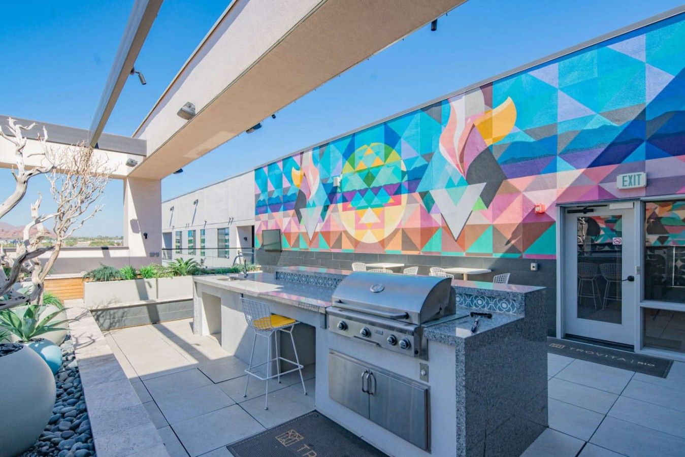 Un patio exterior con una parrilla, zona de estar y un llamativo mural geométrico.