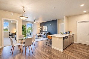 A modern kitchen with a central island, a dining area with chairs, and a living room with a sofa and a ceiling fan. - Heart of Tempe  Balcony, Pool, Gym, WD, Parking (Tempe)