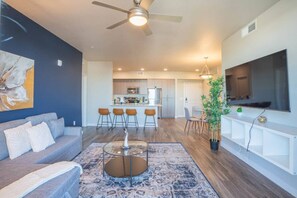 A modern living room with a sofa, coffee table, and a dining area with chairs. - Heart of Tempe  Balcony, Pool, Gym, WD, Parking (Tempe)