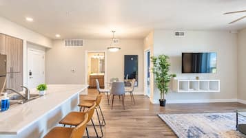 A modern kitchen with a bar area, dining space, and a living area with a TV.