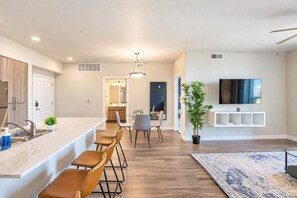 A modern kitchen with a bar area, dining space, and a living area with a TV. - Heart of Tempe  Balcony, Pool, Gym, WD, Parking (Tempe)