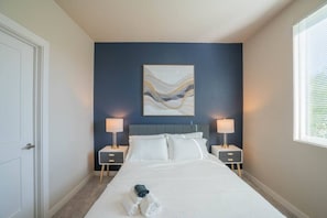 Ein Hotelzimmer mit einem Bett, zwei Nachttischen, einem Wandbild und einem Fenster mit Jalousien.
