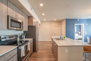 A modern kitchen with a microwave, oven, and refrigerator. There is a dining area with a table and chairs.