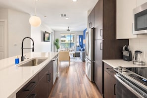 A modern kitchen with stainless steel appliances, a white countertop, and a dining area with a blue accent wall.