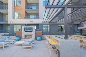 A modern outdoor seating area with a flat-screen TV, lounge chairs, and a fire pit.