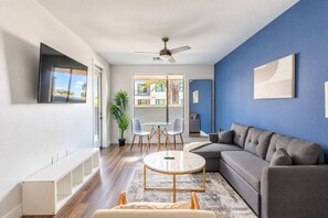 A modern living room with a grey sofa, a round coffee table, and a dining area with a glass table and chairs. - Bright & Sleek 1BR | Parking + Workspace (Tempe)