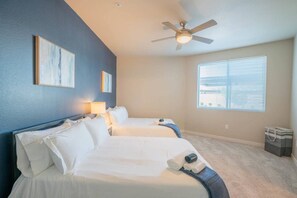 A hotel room with two beds, a ceiling fan, a window with blinds, and artwork on the walls.