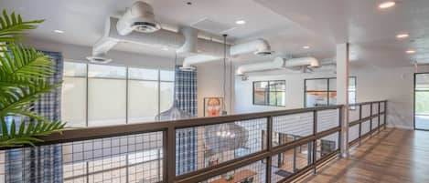 A spacious indoor area with a high ceiling, visible ductwork, and a railing overlooking a lower level.