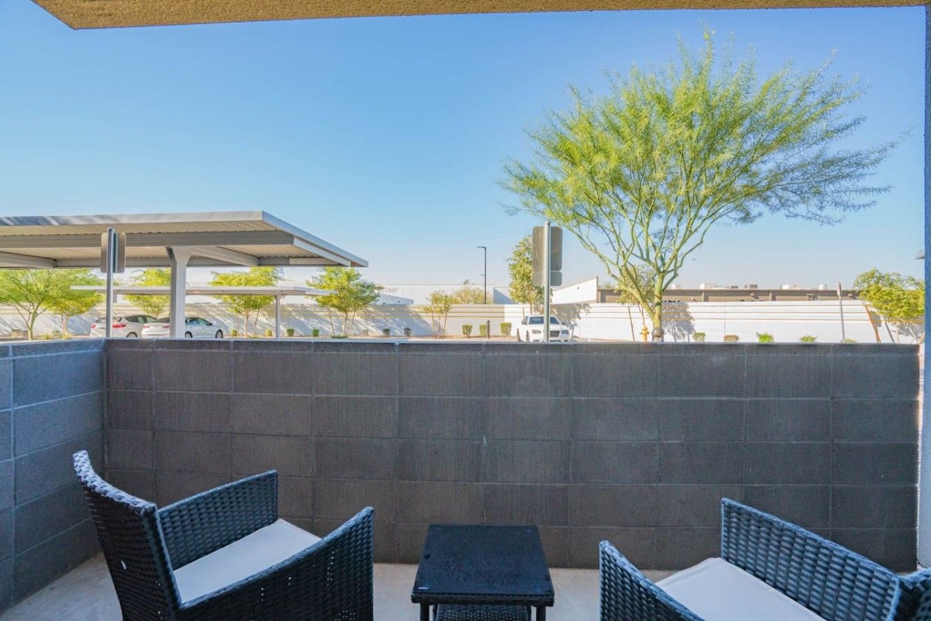 Un espacio al aire libre con mobiliario de mimbre y vistas a un estacionamiento y edificios.