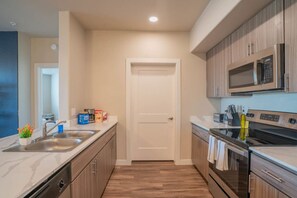 A modern kitchen with stainless steel appliances, wooden cabinets, and a white countertop.