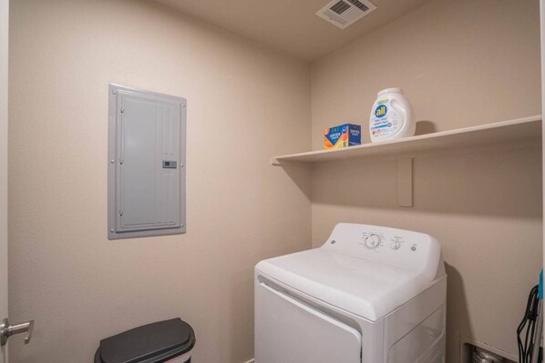 A laundry room with a washing machine, a dryer, and a shelf with detergent.
