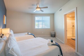 A hotel room with two beds, a ceiling fan, a window with blinds, and a door leading to a bathroom.