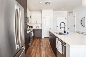 A modern kitchen with stainless steel appliances, white cabinetry, and a wooden floor.
