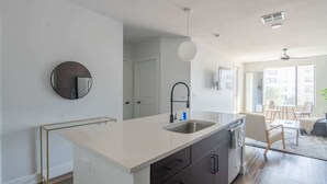 A modern kitchen with a white countertop, dark cabinets, and a round mirror.