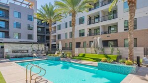 A modern building with a swimming pool, palm trees, and a well-maintained garden.