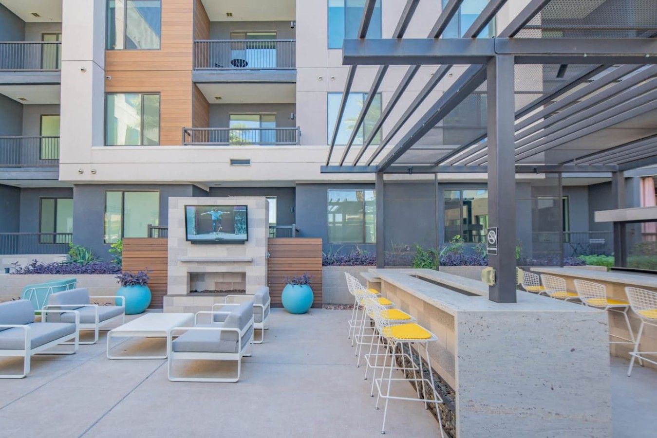 A modern outdoor lounge area with seating and a TV screen, surrounded by balconies and a covered walkway.