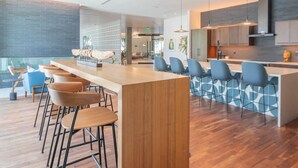 A modern bar area with wooden bar stools and blue chairs, a kitchen with grey cabinets, and a patterned wall.