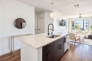 A modern kitchen with a central island, a round mirror, a pendant light, and a view of the city through large windows.