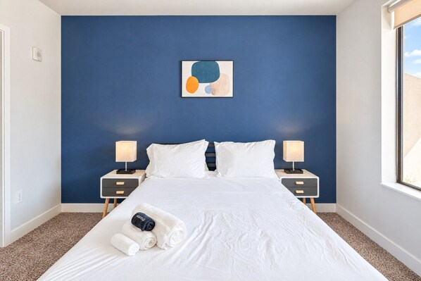 A hotel room with a large bed, two bedside tables, a wall art piece, and a window.