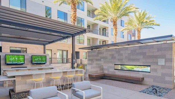 An outdoor seating area with a bar, multiple screens, and a view of a building with palm trees.