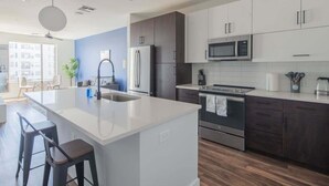 A modern kitchen with a central island, dark cabinets, stainless steel appliances, and a large window.