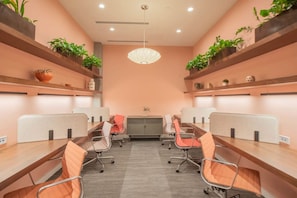 A conference room with a long table, individual workstations, and potted plants on shelves.