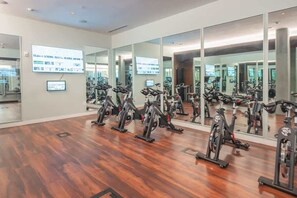Une salle de sport équipée de plusieurs vélos d’exercice, de miroirs aux murs et d’un plancher en bois.