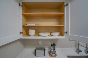 A kitchen with a built-in cabinet containing white plates and bowls, a toaster, and a coffee maker on the countertop.