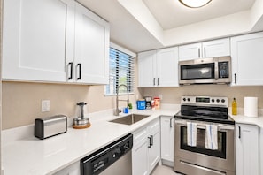 A modern kitchen with white cabinetry, a built-in microwave, an oven, a toaster, and a coffee maker.