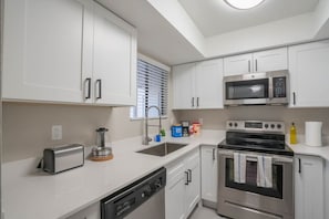 A modern kitchen with white cabinets, a built-in microwave, a stove, and a dishwasher.