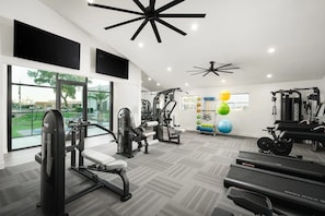 A gym with exercise equipment, large windows, and a ceiling fan.