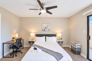 A hotel room with a bed, desk, chair, two bedside tables with lamps, a ceiling fan, and a window.