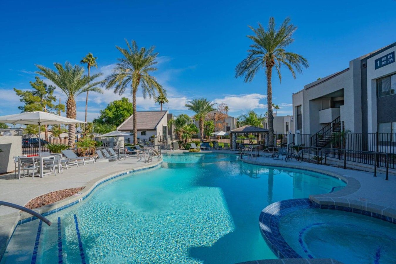 A swimming pool with lounge chairs and palm trees, surrounded by buildings.