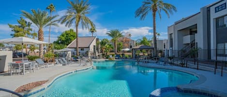 A swimming pool with lounge chairs and palm trees, surrounded by buildings.