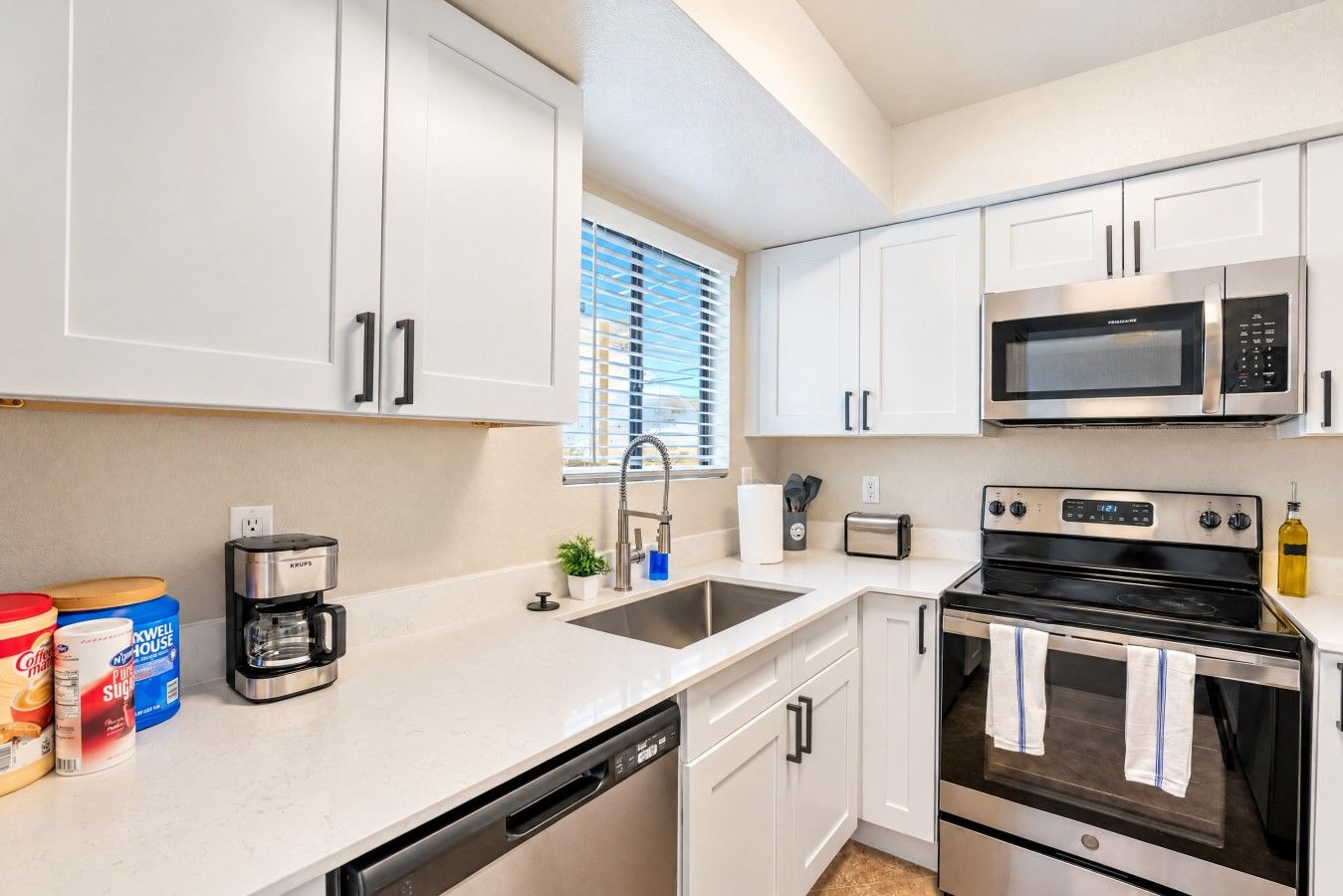 A modern kitchen with white cabinetry, a built-in microwave, a stove, and a dishwasher.