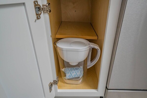 A compact toilet with a transparent tank and a wooden shelf above it.