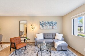 A living room with a grey sofa, a brown leather chair, a glass coffee table, and a painting on the wall.