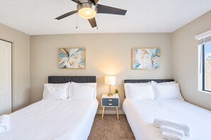 A hotel room with two beds, a ceiling fan, a nightstand with a lamp, and artwork on the walls.