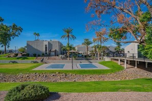 A courtyard with a tennis court, palm trees, and a modern building with a flat roof. - Walk to Old Town Gym, Pool, WD, Pkg  Balcony (Scottsdale)