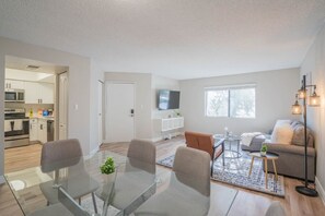 A modern living room with a glass dining table, a sofa, and a TV mounted on the wall. - Walk to Old Town Gym, Pool, WD, Pkg  Balcony (Scottsdale)