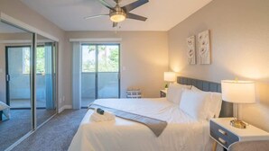 A hotel room with a bed, a nightstand, a lamp, a ceiling fan, and a sliding glass door leading to a balcony. - Walk to Old Town Gym, Pool, WD, Pkg  Balcony (Scottsdale)