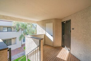 A balcony with a wooden floor, a metal railing, a door, and a view of a building with windows and greenery. - Walk to Old Town Gym, Pool, WD, Pkg  Balcony (Scottsdale)