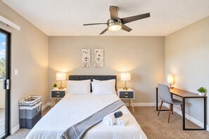 Ein Hotelzimmer mit einem Bett, zwei Nachttischen mit Lampen, einem Schreibtisch mit Stuhl, einem Deckenventilator und Bildern an der Wand.