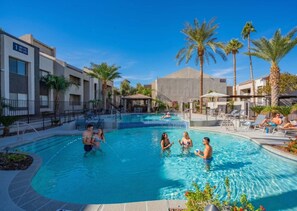 A swimming pool with people in the water, surrounded by palm trees and buildings. - Walk to Old Town Gym, Pool, WD, Pkg  Balcony (Scottsdale)