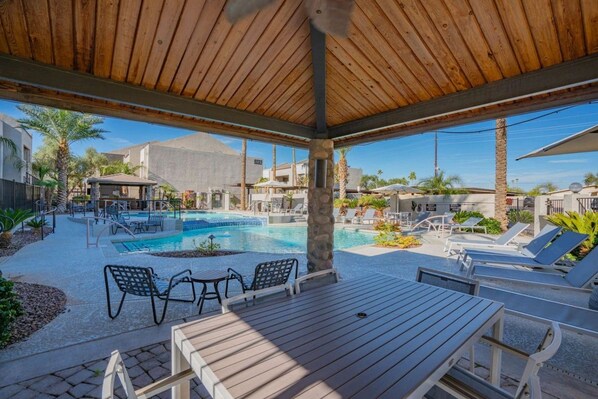 A pool area with lounge chairs and a covered seating area.