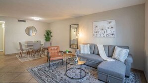 Ein modernes Wohnzimmer mit einem grauen Sofa, einem runden Couchtisch und einem Essbereich mit einem Glastisch und Stühlen.