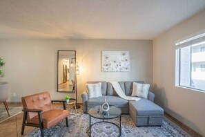 A living room with a grey sofa, a brown leather chair, a round coffee table, and a large mirror.
