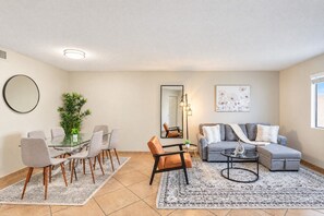 A modern living room with a dining area, a sofa, a coffee table, and a large mirror. - Near DT & Trails | Pool,Gym,Balcony,W/D,Parking (Scottsdale)