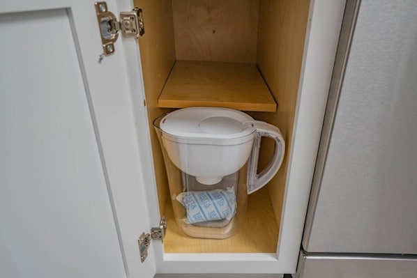 A compact toilet with a transparent tank and a wooden shelf above it.