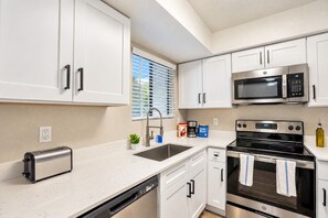 Een moderne keuken met witte kasten, een RVS magnetron, een inbouwoven en een vaatwasser.